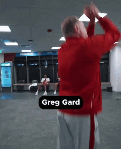 a man in a red jacket is dancing in a room with greg gard written on the bottom