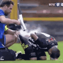 a referee is kneeling down on the field while another man holds a baseball bat