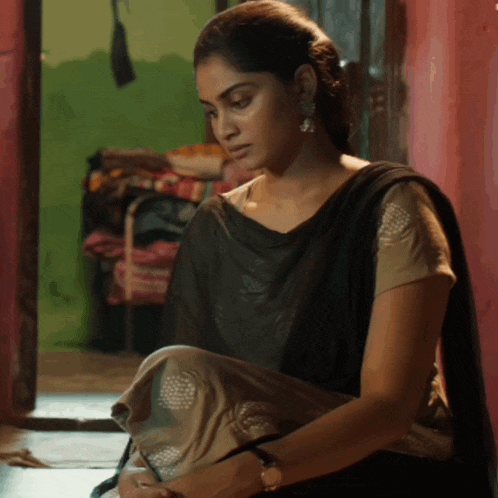 a woman in a black saree sits on the floor looking down