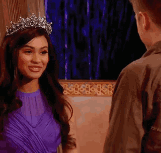 a woman wearing a tiara and a purple dress is smiling at a man