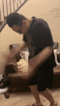 a man in a black shirt and shorts is standing in front of a couch in a living room .