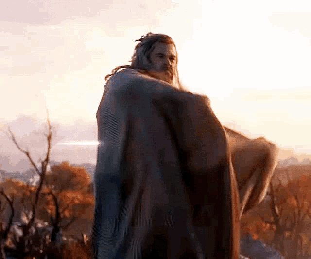 a man wrapped in a blanket is standing in the woods .