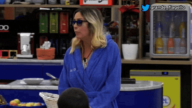 a woman in a blue robe and sunglasses stands in front of a refrigerator that says grande flagello on it
