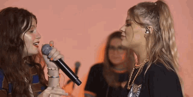 a woman singing into a microphone while another woman looks on .