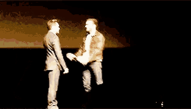 two men are standing next to each other on a stage and one of them is jumping in the air .
