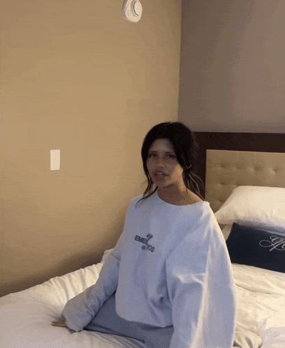 a woman sits on a bed wearing a sweatshirt that says emporio armani