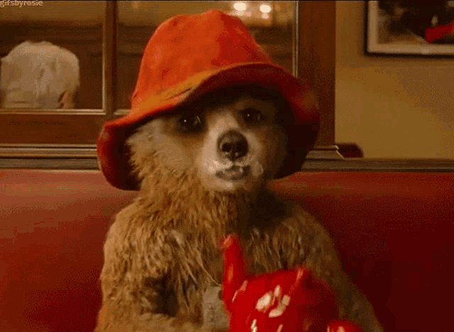 a teddy bear wearing a red hat is drinking from a red teapot