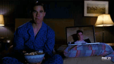 a man is eating popcorn in front of a laptop that says fox 25 on it