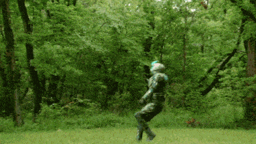 a man in a green suit is standing in a field with trees in the background and a red figure in the background