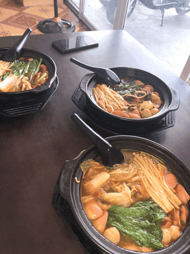three bowls of food on a table with a phone on the table