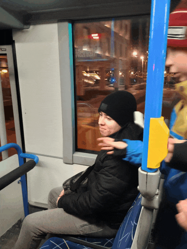 a man in a black hat sits on a bus next to a blue pole with a yellow sticker on it