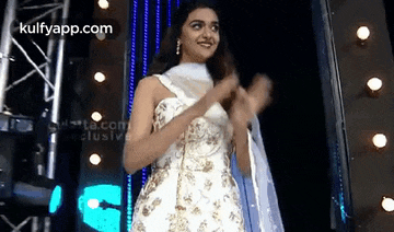 a woman in a white dress is standing in front of a stage and clapping .