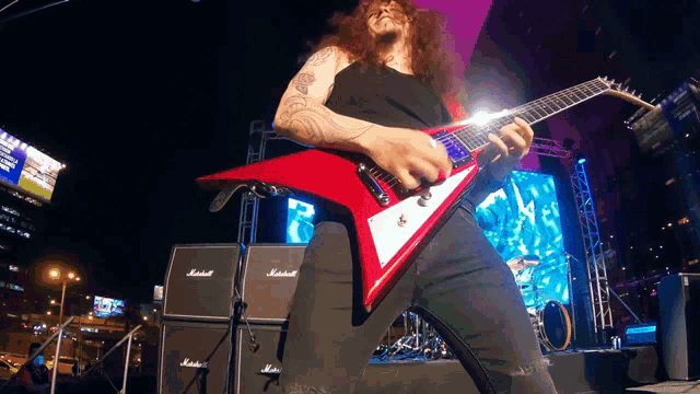 a man plays a red guitar in front of a marshall amplifier