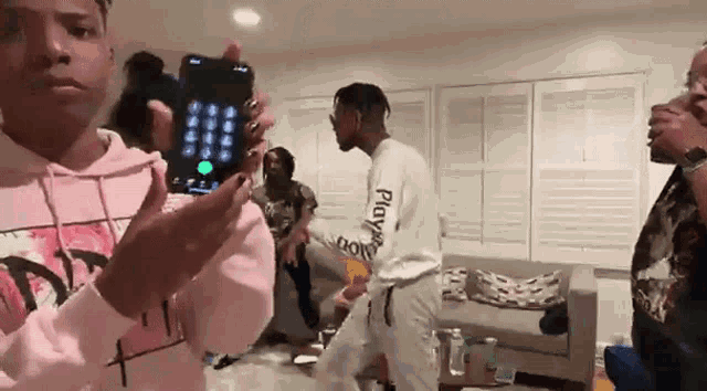 a group of people are dancing in a living room while a man holds a cell phone in his hand .