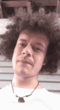 a man with curly hair is wearing a white shirt and a black necklace .