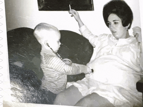 a black and white photo of a baby playing with a stethoscope on a pregnant woman 's belly