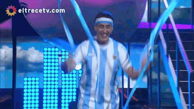 a man in a blue and white shirt is dancing in front of a eltrecetv.com logo