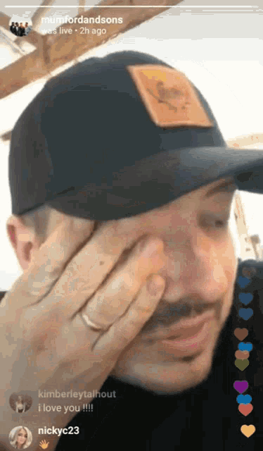 a man wearing a black hat is covering his face with his hand and a ring on his finger