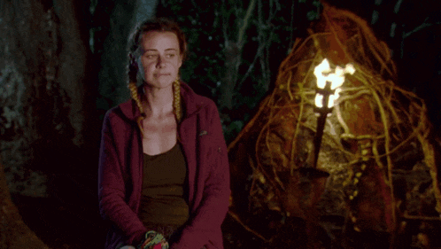 a woman in a purple jacket stands in front of a lit torch