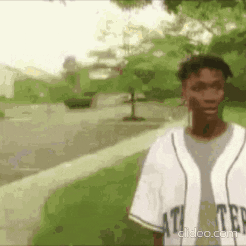 a man in a baseball uniform is standing on a sidewalk in a park .