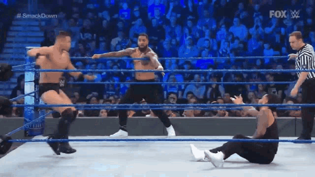 two wrestlers are fighting in a wrestling ring while a referee watches .