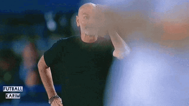 a bald man in a black shirt stands in front of a blue background with the words futbol karim written on it