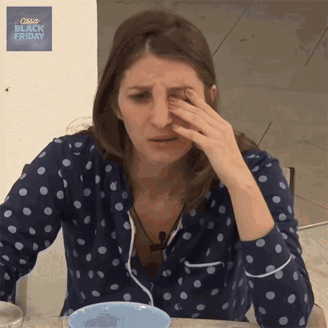a woman wearing polka dot pajamas wipes her eyes with her hand