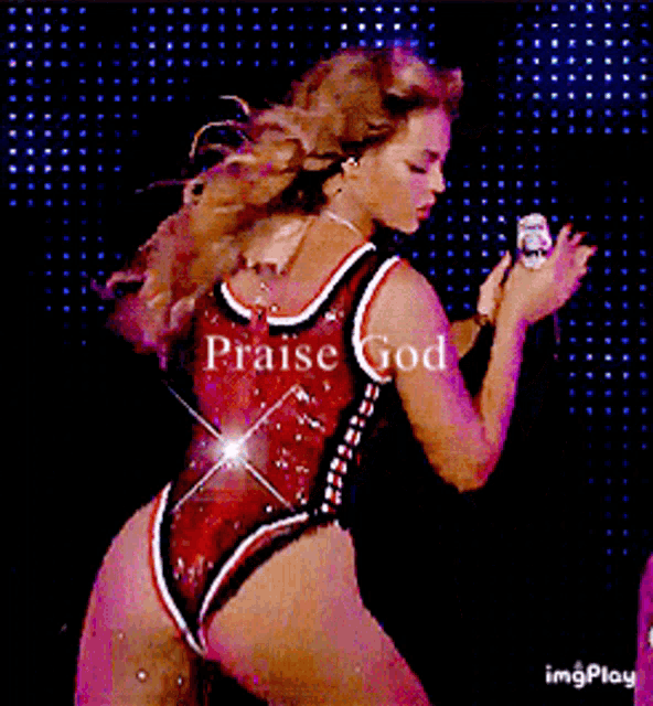 a woman in a red bodysuit is holding a microphone and says praise god .