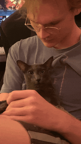 a man with glasses is holding a cat in his lap