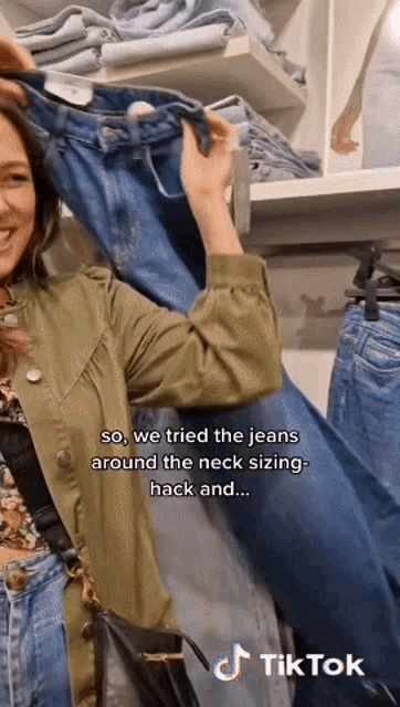 a woman in a green jacket is holding a pair of jeans in front of a rack of jeans