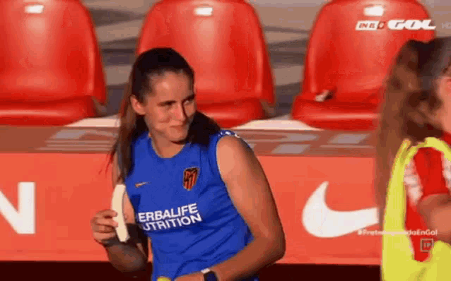 a woman in a blue shirt is holding a banana while standing on a soccer field .