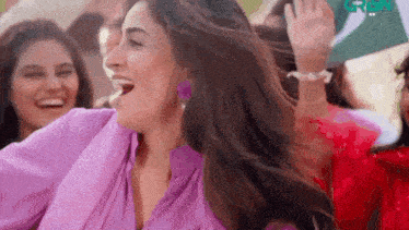 a woman in a purple shirt is dancing with her hair blowing in the wind while another woman looks on .
