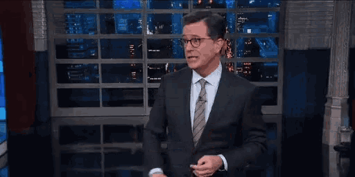 a man in a suit and tie is waving his hand and saying `` bye '' on a stage .