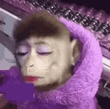 a monkey wearing a purple sweater and lipstick is sitting on a table .