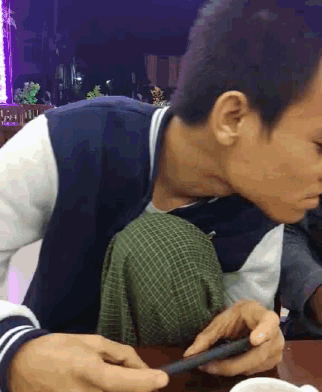 a young man is sitting at a table looking at his phone