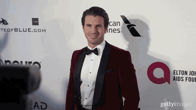 a man in a red tuxedo is standing in front of an elton john aids four logo