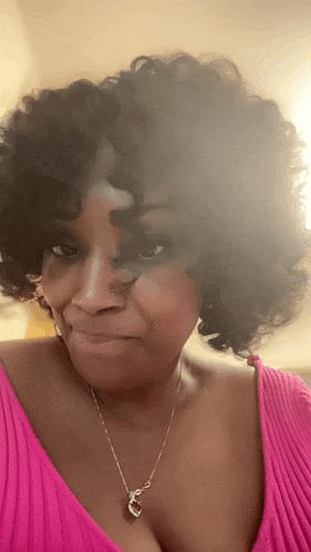 a woman with curly hair wearing a pink top and a silver necklace