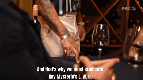 a man with a tattoo on his arm talks to another man with a glass of wine