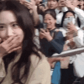 a woman is covering her mouth in front of a crowd of people