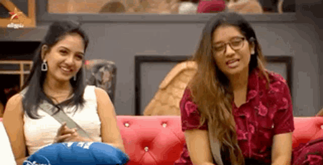 two women are sitting on a red couch and smiling .