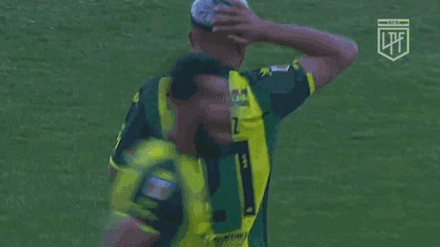 a soccer player wearing a green and yellow jersey with the number 21 on it holds his head in his hands .