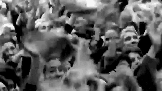 a black and white photo of a crowd of people holding their hands up in the air .