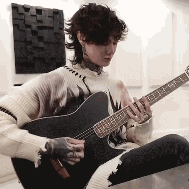 a man in a sweater is playing a black guitar