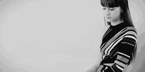 a woman in a striped sweater is standing in front of a white wall in a black and white photo .