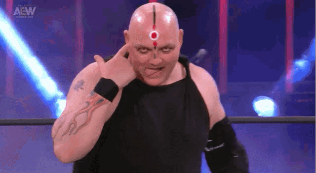 a bald wrestler with a tattoo on his arm and a red circle on his forehead is making a funny face
