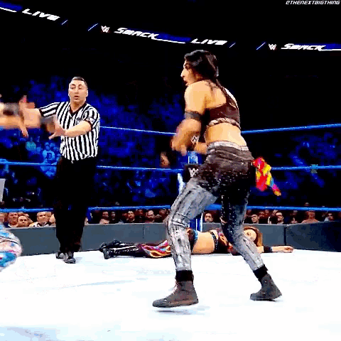 a woman is standing in a wrestling ring with a referee standing behind her .