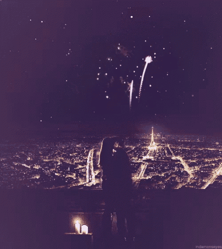 a couple kissing in front of a fireworks display with a candle in the foreground