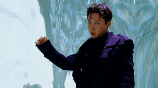 a young man in a purple suit is standing in front of a white wall .