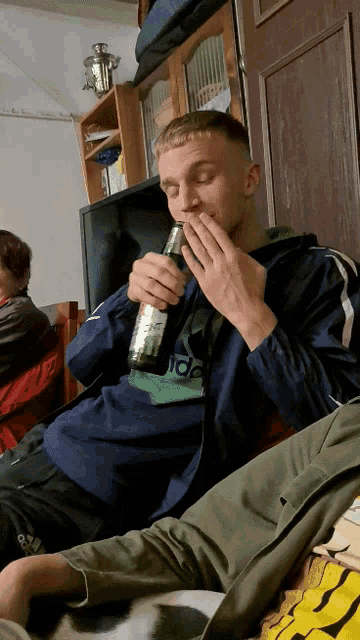 a man wearing an adidas jacket holds a bottle of beer