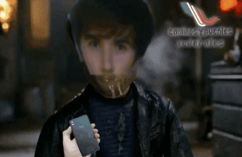 a man with a mask on his face is holding a cell phone with caminos y puentes federales on the bottom